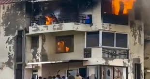Burnt residential building in Dwarka with flames visible on balconies and windows, showing the aftermath of a fatal apartment fire.