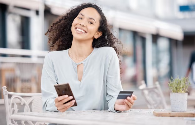 A confident young woman using a mobile finance app at a café, smiling with empowerment. (Alt text: Empowered Indian woman managing finances on her phone with Vizzve Finance)