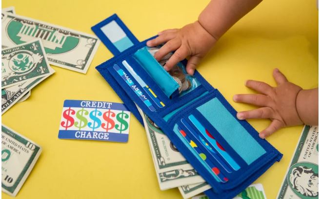 A parent and child sitting at a table discussing money with coins, a notebook, and a piggy bank in front of them