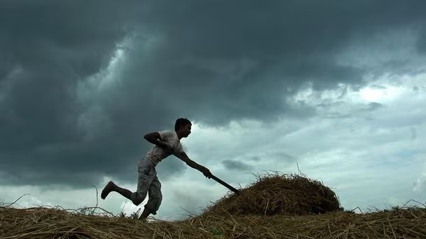 Indian farmer in a field under monsoon clouds with financial graphs showing market trends, used by Vizzve Finance to illustrate economic impact