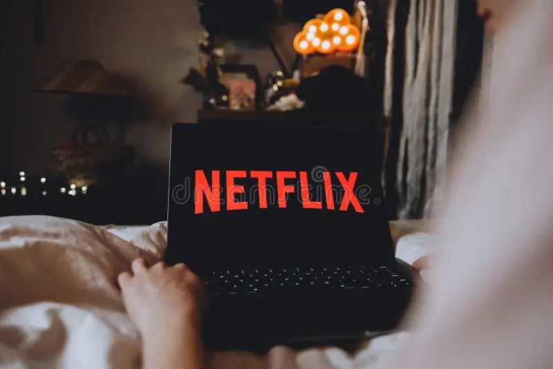 Person watching Netflix on laptop with EMI symbols and digital wallet icons