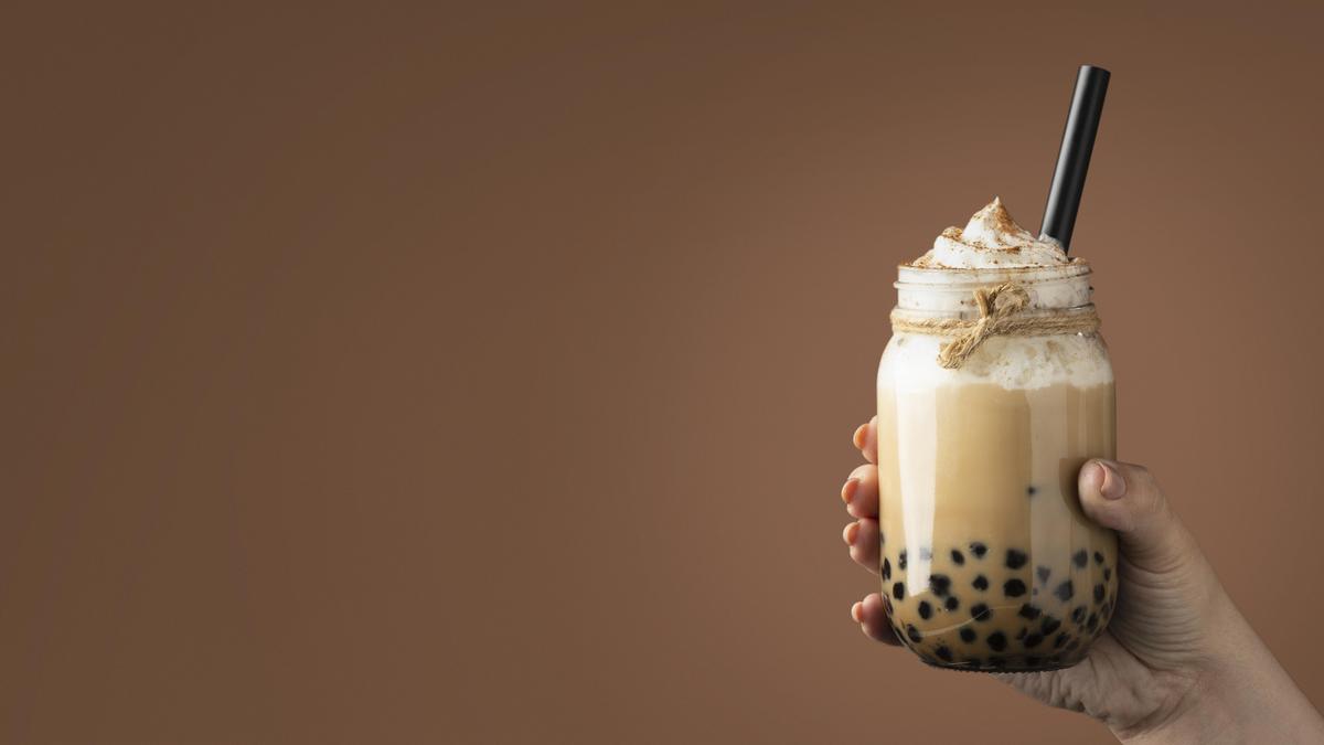 Close-up of a bubble tea drink with tapioca pearls and a wide straw in a clear cup.