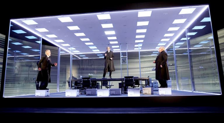Three actors on stage in a minimalist set, portraying the Lehman Brothers across time