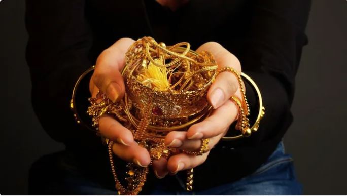 "Gold jewelry and coins locked in a safe with financial documents and calculator on the table"