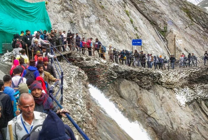 Amarnath pilgrims walking in rocky terrain with landslide warning