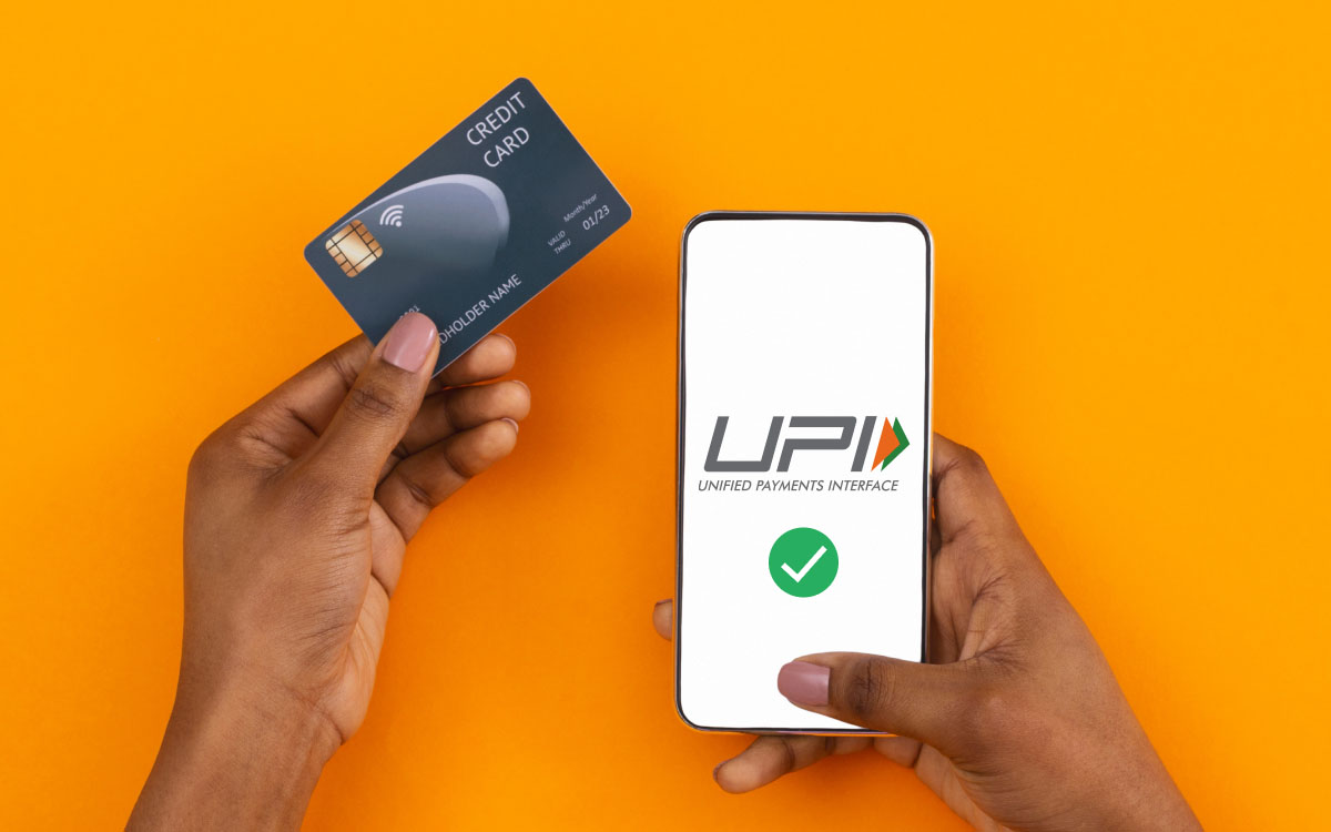 A person scanning a QR code with a smartphone labeled “Credit via UPI,” with icons for Visa, Mastercard, RuPay, and Paytm