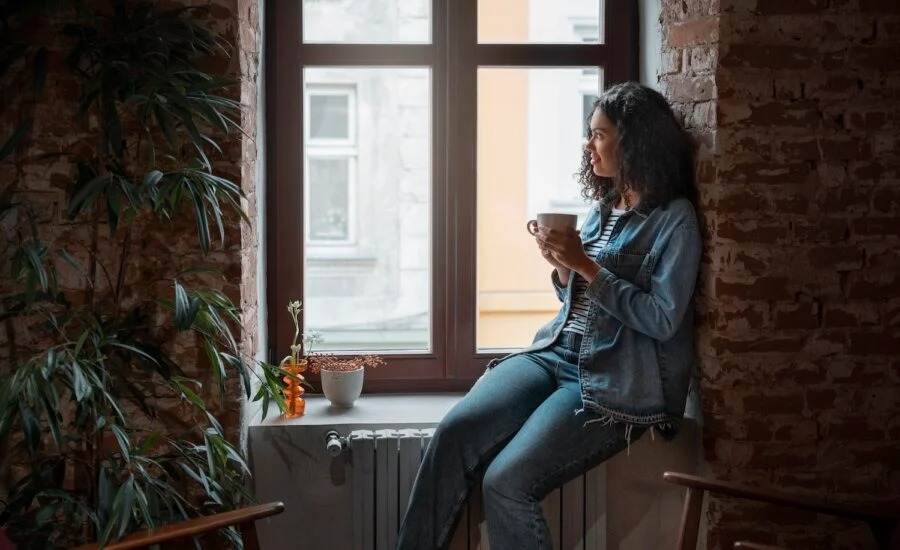 A young millennial relaxing in a cozy apartment with budget notes and coffee. Text overlay: “Smart Solo Living Under Budget – Vizzve Lifestyle Tips”.