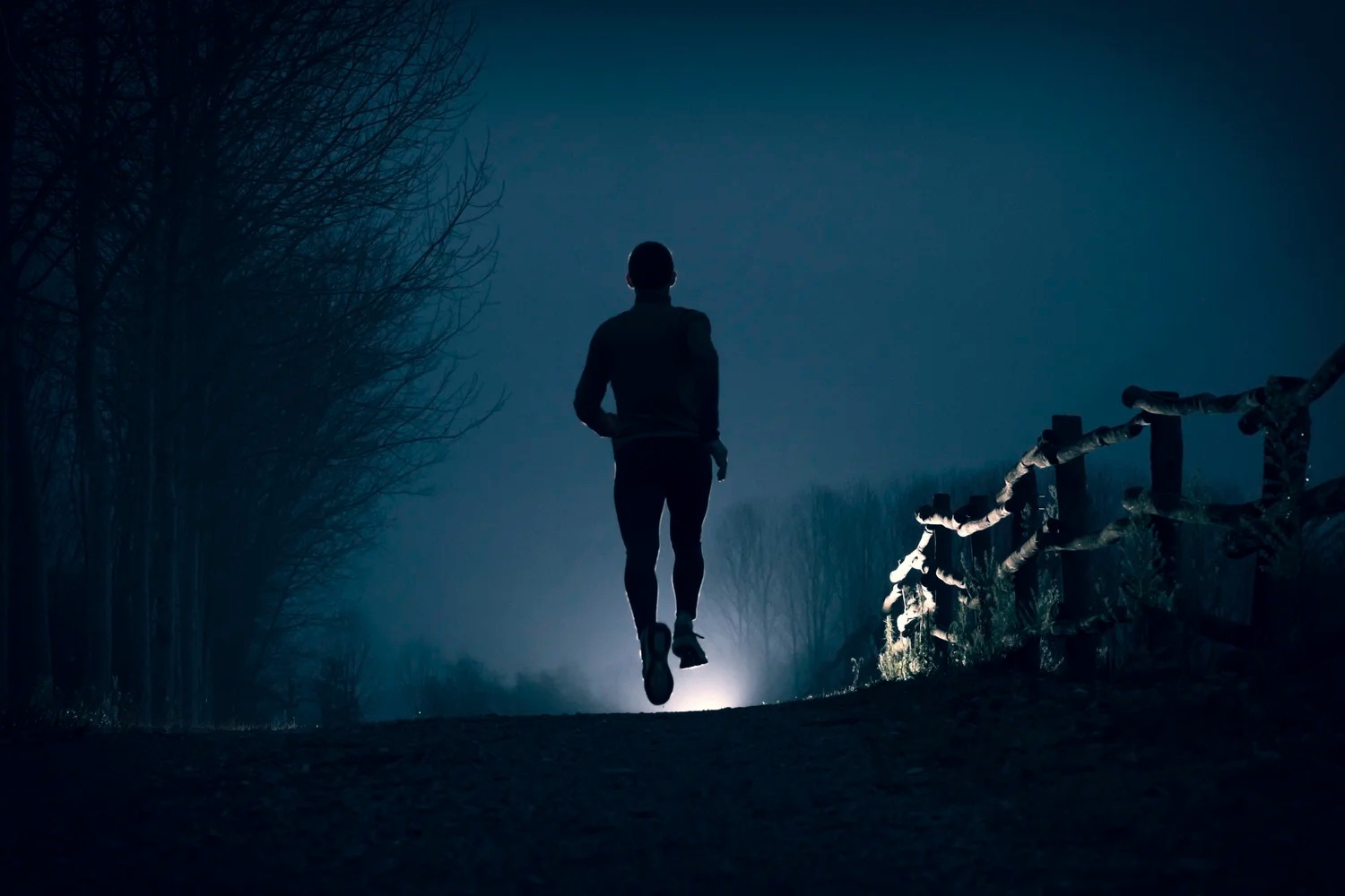 A person running on a track alone in the dark, with a spotlight ahead symbolizing future victory.