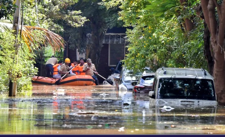 Flooded streets in an Indian city during heavy monsoon rains, with waterlogged vehicles and people navigating the water