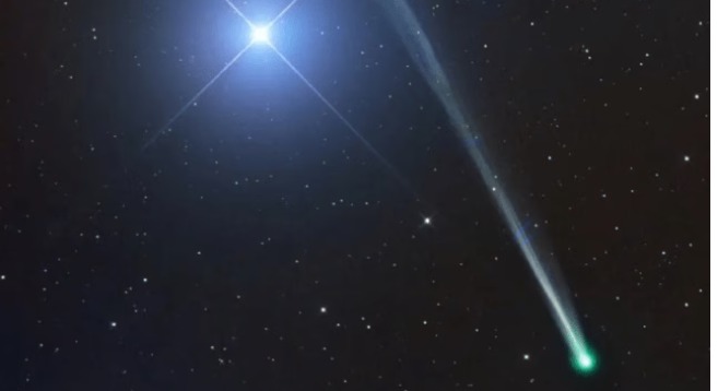 Comet C/2025 R2 (SWAN) with its greenish coma and tail against a starry background.