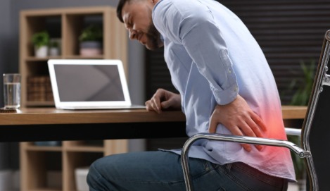 Person sitting at desk using laptop with poor posture, increasing arthritis risk.