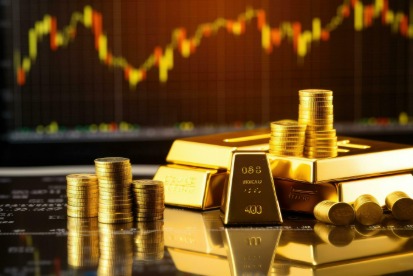 Gold bars and coins placed on fluctuating stock market chart.