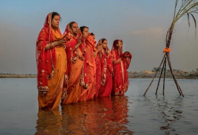 Devotees performing Chhath Puja rituals at sunrise on a riverbank.