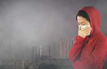 Woman wearing mask coughing outdoors due to air pollution in Delhi.
