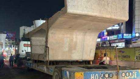 Damaged car wreckage after crashing into a Pune Metro pillar at night, with police and rescue workers at the scene