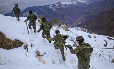 Indian Army soldiers conducting surveillance along the Line of Control in Jammu & Kashmir, with mountainous terrain and forward posts in background