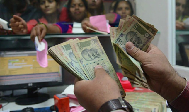 Person depositing a large amount of cash at a bank counter with bank officer accepting documents