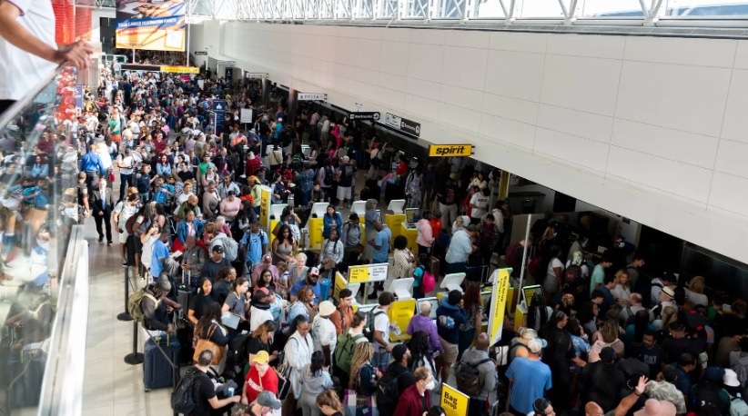 Passengers at a busy U.S. airport terminal checking flight information boards showing delays and cancellations.