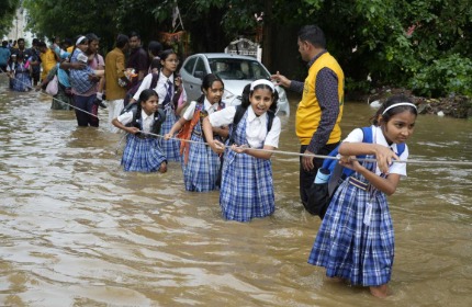 Students walking with umbrellas outside school premises during rainy weather in Chennai.