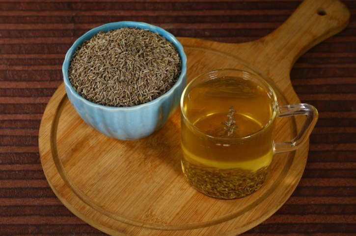 Glass of jeera water with soaked cumin seeds on a wooden table