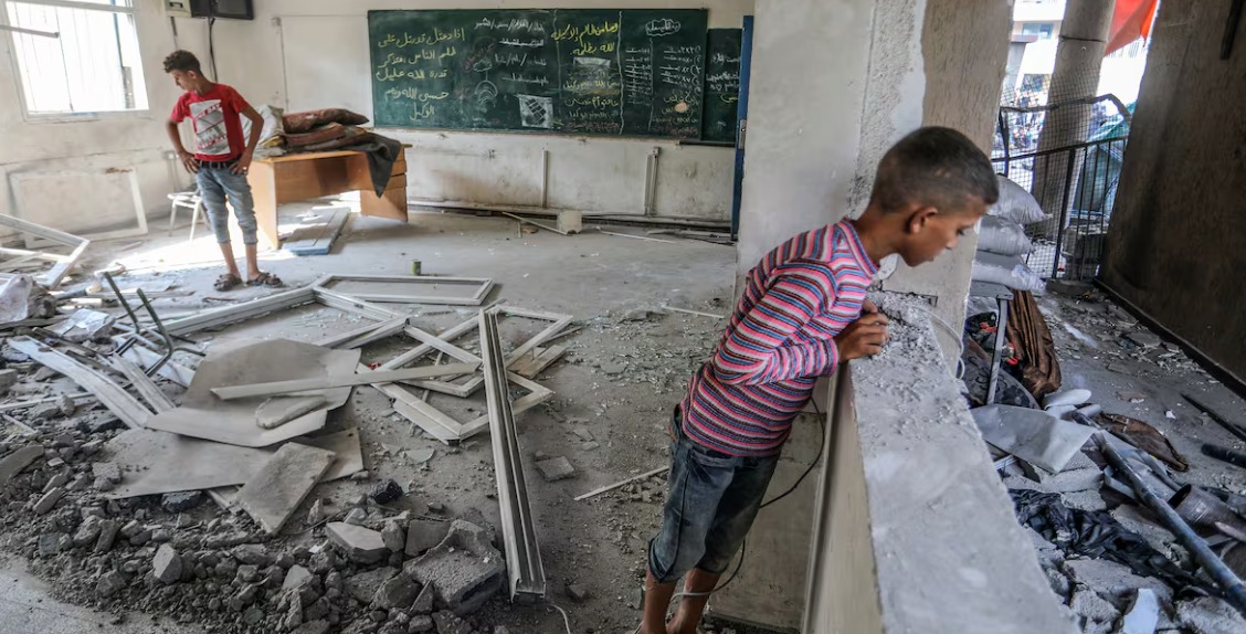 Children in Gaza sitting on the ground in makeshift classroom with no chairs or books
