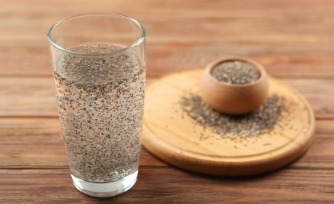 A glass of warm ajwain water with carom seeds on a wooden table